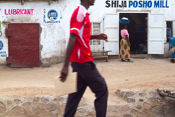 Mwanza, Tanzania: Woman at Mill with Parcel on Head Mwanza, Tanzania - May 15, 2012: A woman in traditional dress with a parcel on her head at a flour mill. A man is walking by in the foreground. mwanza city tanzania stock pictures, royalty-free photos & images