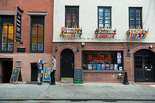 New York City, USA - July 14, 2016: Two people stand outside the Stonewall Inn, a gay bar in the Greenwich Village neighborhood of New York City. In June 2016, President Obama established a 7.7-acre area around the site as the Stonewall National Monument, America's first LGBT national park site.