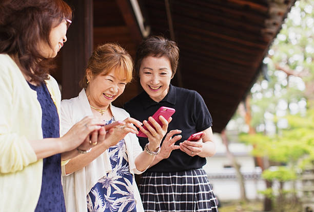Senior Japanese Women Looking at Pictures on Phone Three senior Japanese women and friends are looking at the pictures taken with their mobile phones. They are smiling and having a great time exploring the new frontier of social media. Image taken in Kyoto, Japan. kyoto prefecture photos stock pictures, royalty-free photos & images