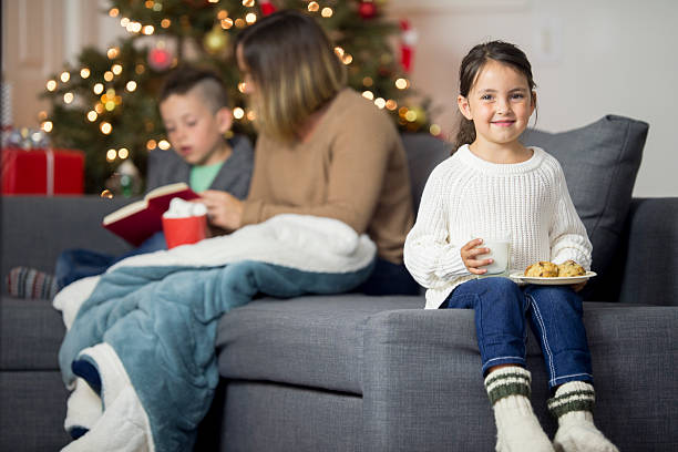 Holding Milk and Cookies A little girl has milk and cookies to leave for Santa on Christmas eve. Her mother and brother and sitting in the background by the tree. long sleeved recreational pursuit horizontal looking at camera stock pictures, royalty-free photos & images