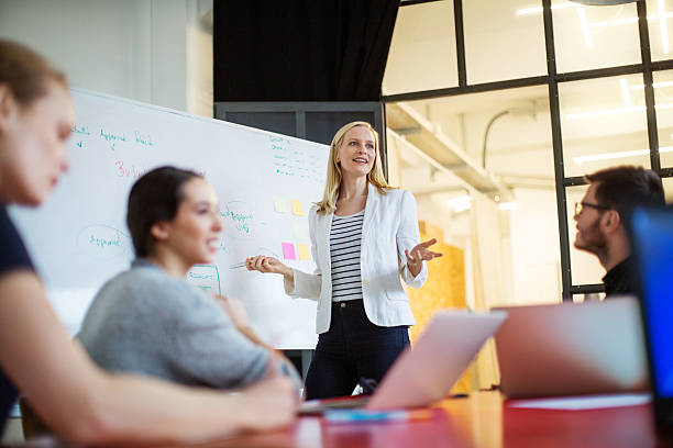 Businesswoman giving presentation on future plans to colleagues Young businesswoman giving presentation on future plans to her colleagues at office marketing meeting stock pictures, royalty-free photos & images