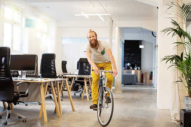 Happy young man cycling in a startup Happy young man cycling through a startup office hipster bike stock pictures, royalty-free photos & images