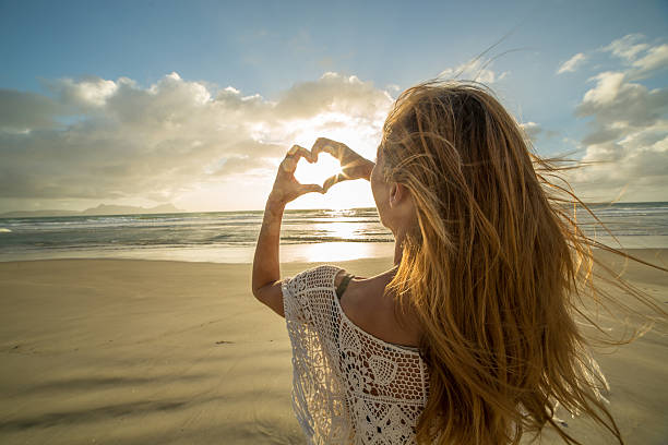 istock Woman on beach makes heart shape finger frame to sunset 576906184