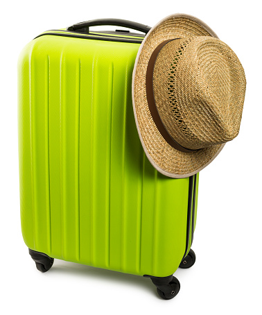 For travel and vacations purposes, a simple modern suitcase in fluorescent green color, with a male straw hat sitting on top of it, is nicely isolated on a pure white background.