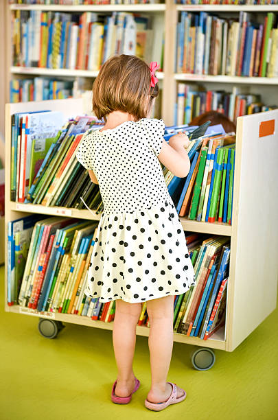 Little girl is choosing a book in the library. A child is looking at the books in the library deciding which one to take home. Children creativity and imagination.