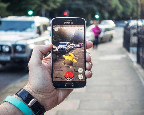 Playing Pokemon Go on the street Edinburgh, UK - July 18, 2016: Closeup of a man holding a Samsung S6 smartphone, playing Pokemon Go with the game's augmented reality superimposing a character onto the pavement surface, as a person approaches in the distance. brand name games console stock pictures, royalty-free photos & images