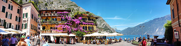 Limone del Garda, Italy - July 17, 2016: Panoramic view of Piazza Garibaldi - Limone is one of most famous locations of Garda Lake. Many poeple walking on Garibaldi Square. On the right the fountain with many flowers. Some tourists are sitting on restaurant. Other people looking for the shopping.