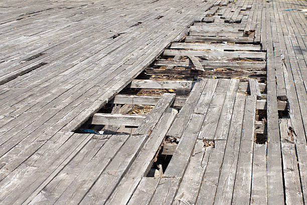 The pit (hole) in the old and worn floor. The material covering the wood. The flooring is gray. Around lie fragments (pieces) of wooden planks.