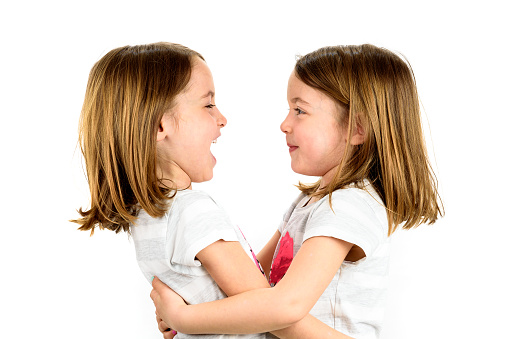 Twin girls are looking at each other and smiling. Concept of family and sisterly love. Profile side view of sisters playing.