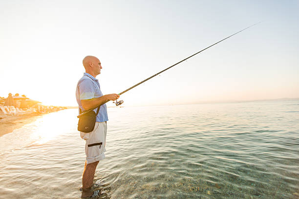 A man crouching on the beach while fishing