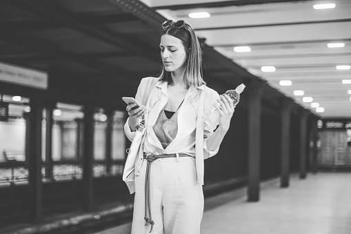 Young woman is texting on the subway station while she is waiting the metro