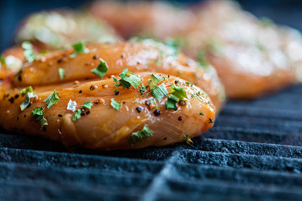 Raw marinated chicken breasts cooking on the BBQ grill.