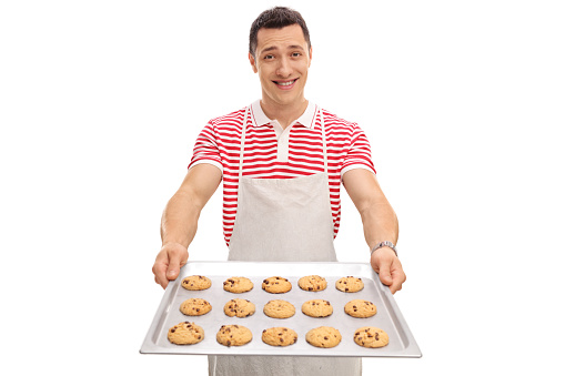 Cheerful guy holding a tray with homemade chocolate chip cookies isolated on white background
