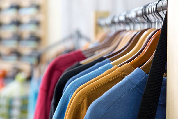 fila de ropa de colores en perchas de la tienda minorista - shirt hanger hanging blue fotografías e imágenes de stock