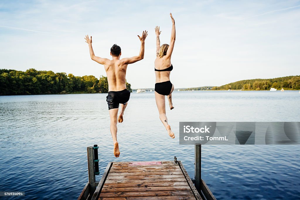 Jumping into the water from a jetty Happy couple jumping into the water from a jetty Jumping Stock Photo