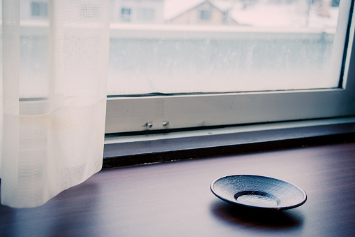 empty saucer of Hot Japan tea cup on wood bar beside window at snowy day, Hakkaido, Japan