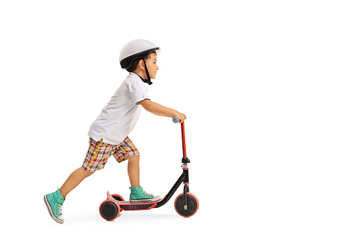 Little boy riding a scooter in a protective helmet isolated on a white background