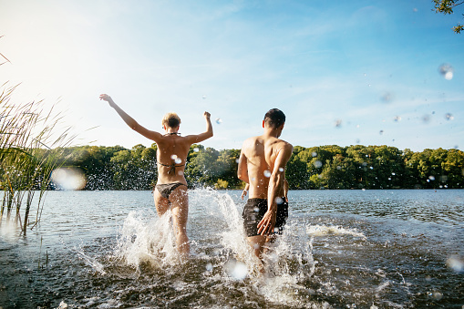 Three young people splashing into a lake and having fun together.