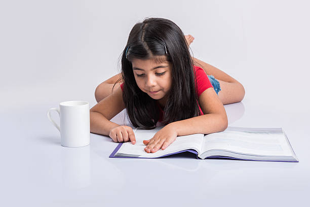 istock indian small girl child reading book on ground 576935516