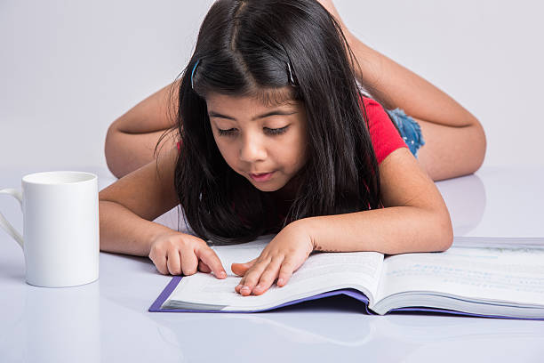 istock indian small girl child reading book on ground 576936200