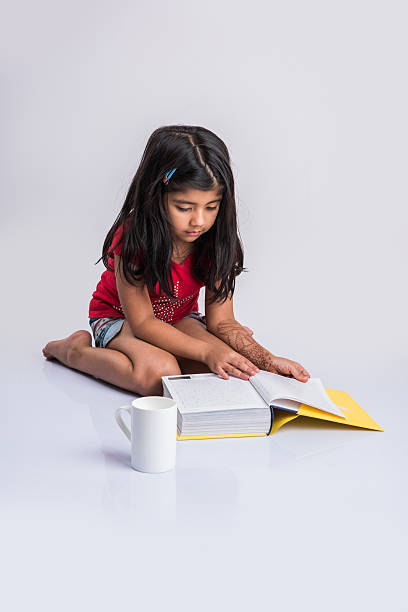 istock indian small girl child reading book on ground 577305192