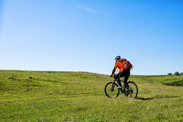 istock Young man cycling on a rural road through green meadow 577308048
