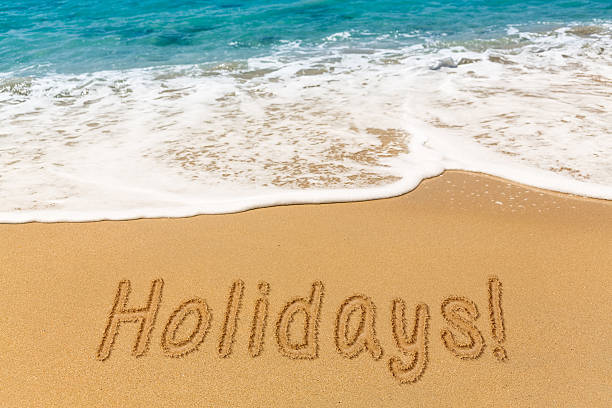 istock Holidays written in sand with sea surf 577309292