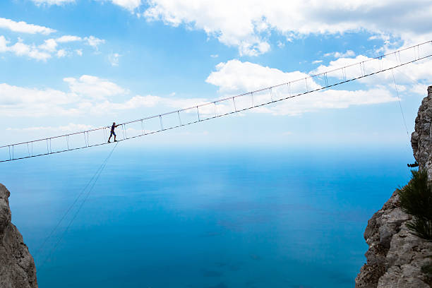 Man climbing on the suspension bridge to the peak of mountain.