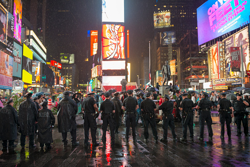 New York City, USA - July 9, 2016: On a wet and rainy night, New York City police officers stand together, facing in the direction of Black Lives Matter protestors who are gathered in Times Square and demonstrating against police violence.