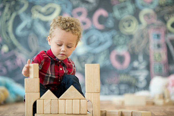 Building a Block Tower A cute little boy is playing on the floor with wood blocks in his preschool classroom. montessori education stock pictures, royalty-free photos & images