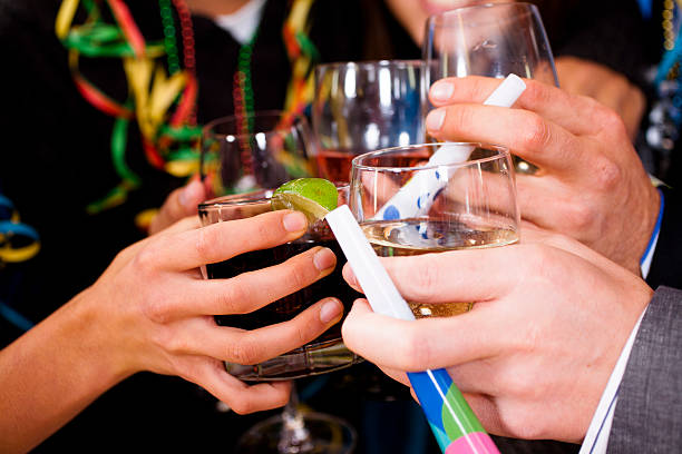 Close up of hands holding various alcoholic drinks make a toast during a celebration event. New Year's Eve celebration or at home party.  Cheers. Party blow horns and streamers.