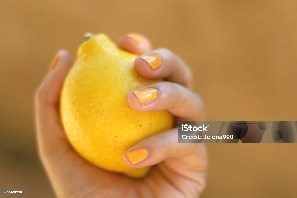 Lemon Hand with yellow nail polish holding a lemon. Selective focus. Cool Attitude Stock Photo