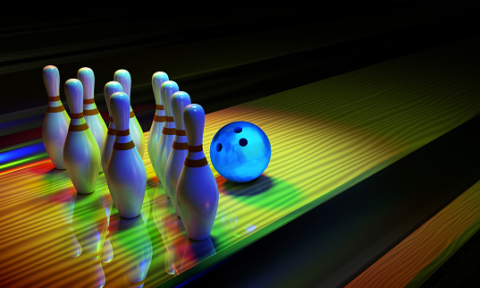 Glossy bowling ball and skittles on the alley. Dark scene with rainbow shining colors.