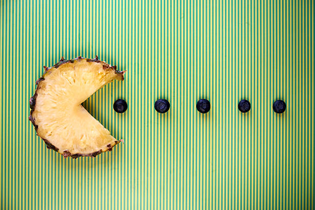 Pineapple slice in the shape of pacman figure eating blueberries