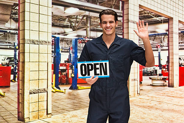 istock Happy mechanic waving  hand while holding open sign 577324246