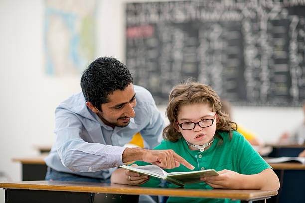 Teacher Assisting a Student A teacher is assisting an elementary age student with a homwork question in his notebook. special education stock pictures, royalty-free photos & images