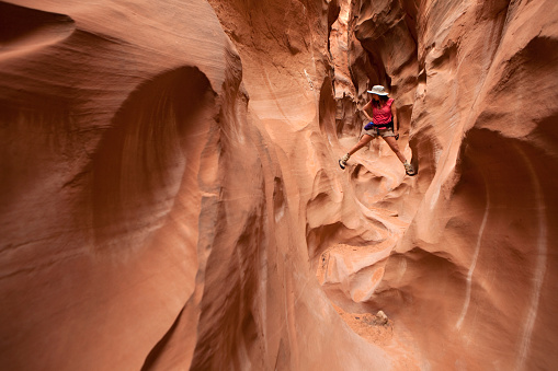 Wedged in between canyon walls, a woman climbs and hikes along the wind and water eroded slot canyon and cliffs of Coyote Gulch in the Escalante National Monument, Utah.