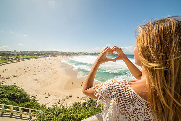 istock Young woman frames Bondi beach into heart shape finger frame 577347030