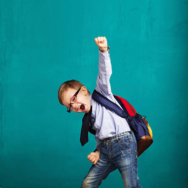 smiling little boy with big backpack jumping and having fun - blackboard education classroom photography imagens e fotografias de stock