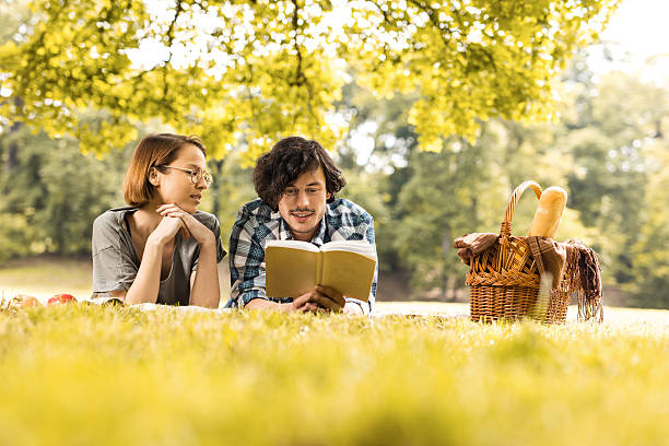 istock Young man reading a book to his girlfriend at picnic. 577616422