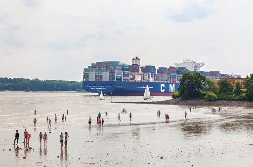 Hamburg, Germany - July 10, 2016: Container ship passing the beach of Wedel, Hamburg. Many people enjoy the warm summer afternoon and observing the huge container ship.