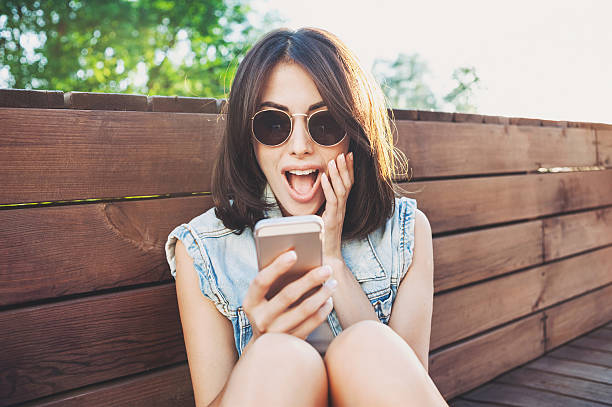 удивленная девушка с помощью смартфона - beautiful communication enjoyment happiness стоковые фото и изображения