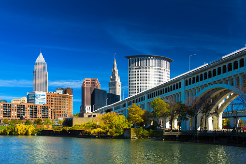 Downtown Cleveland skyline (featuring Key Tower) with the Cuyahoga River, Detroit-Superior Bridge, Autumn colored trees, and a deep blue sky with wispy clouds.  Wide Angle.