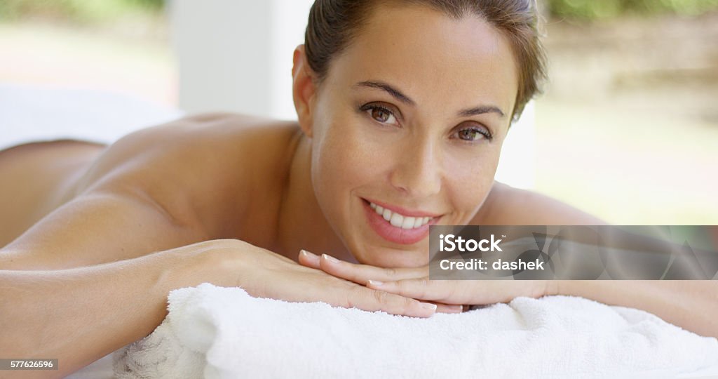 Woman with chin on folded towel smiles Woman with chin on folded towel smiles while laying on massage table in outdoor spa Adult Stock Photo