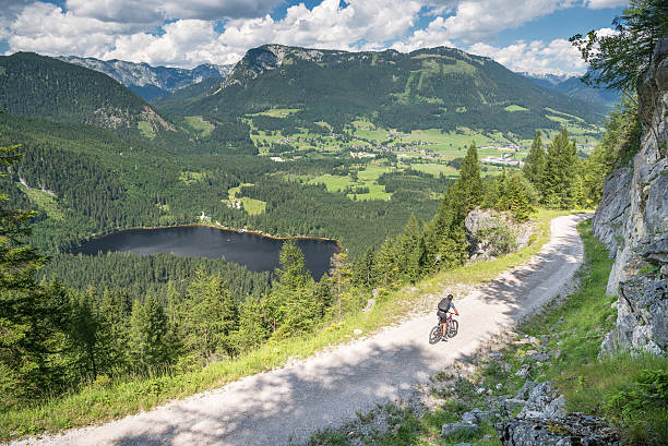 Mountain Bike Trail, Lake Ödensee, Austrian Alps Panorama Man riding down an alpine Mountain Bike Trail, Dachstein Runde, Ödensee, Austrian Alps. Stunning view. Part of the famous Mountain Bike Dachsteinrunde. Nikon D810. Converted from RAW. single lane road footpath dirt road panoramic stock pictures, royalty-free photos & images