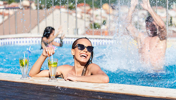 lächelnde junge frau trinkt cocktails im schwimmbad - drink swimming pool cocktail poolside stock-fotos und bilder