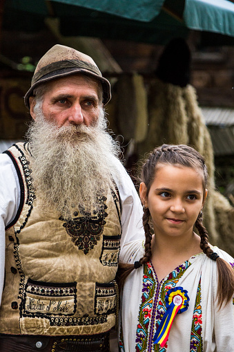 , Bucharest, Romania - May 18, 2016: a tanner (leather maker) and his young daughter stand side by side at a market in the Herastrau area of Bucharest, Romania. They are wearing traditional clothing, and the man has a long grey beard and a hat.