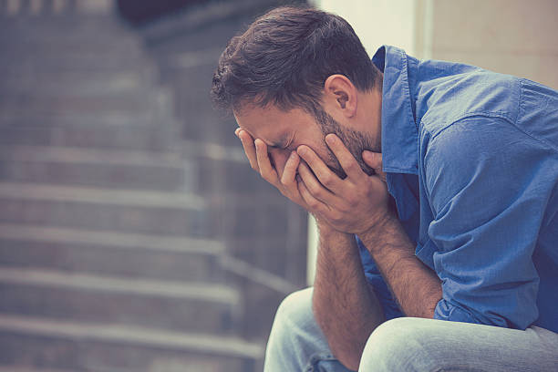 stressed sad crying man sitting outside side profile stressed sad young crying man sitting outside holding head with hands looking down. Human emotion feelings man crying stock pictures, royalty-free photos & images