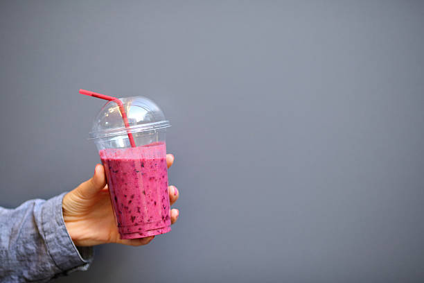 Disposable cup with a Smoothies in woman hand on gray background