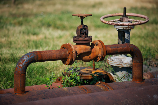 A selective focus of a shiny faucet with an old and rustic pipe against a blurry grass background